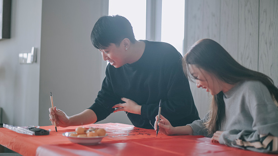 Asian chinese family writing chinese calligraphy on red paper for prosperity and preparing chinese new year home decoration