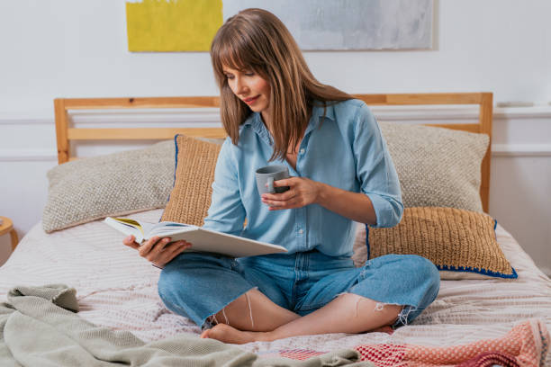 istock Happy Woman Drinking Coffee on her Bed and Reading a Book 1291476463