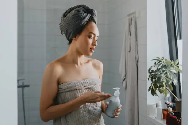 Photo of Young African American Woman Wrapped in a Towel after a Shower Holding a Skin Care Product