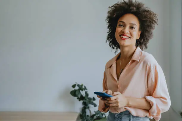 Photo of Portrait of a Smiling African American Woman Using a Smartphone at Home (Copy Space)