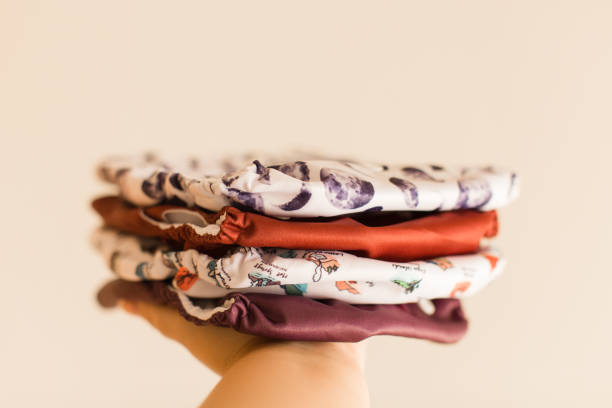 A Woman Holding a Slim Stack of Modern Neutral-Colored Reusable Cloth Diapers with a Neutral Background in Bright Natural Light
