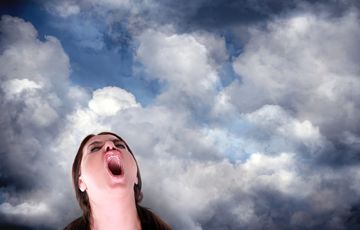 Portrait of close up mid adult woman screaming over dramatic storm clouds