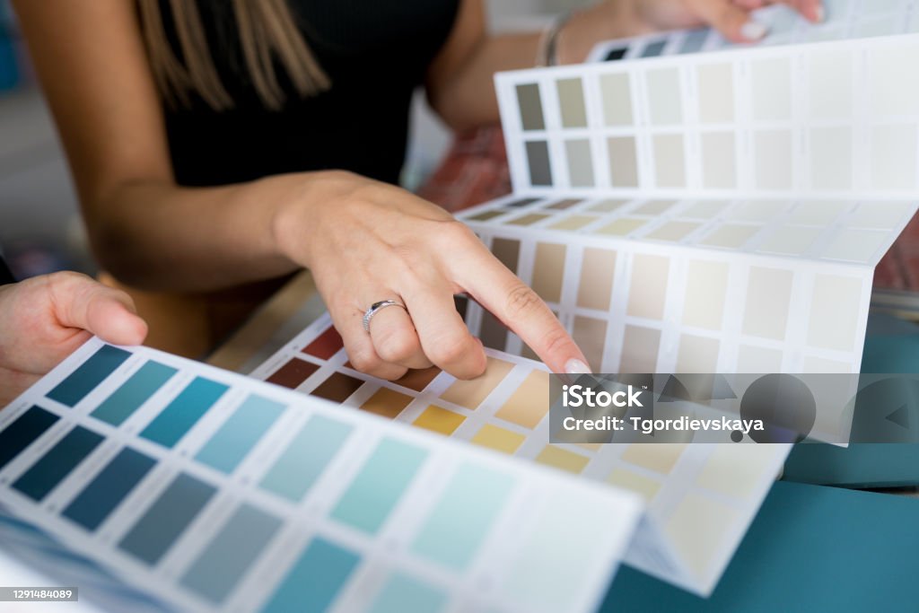 Close-up of two women choosing samples of wall paint. Interior designer consulting a client looking at a color swatch. House renovation concept Paint Stock Photo