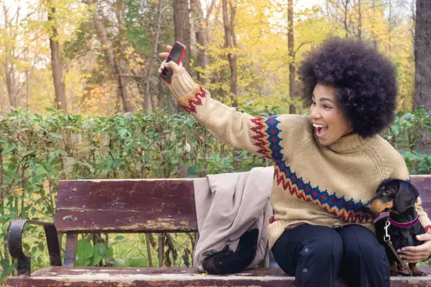 an african american girl sitting on a bench with her dachshund calling her friends