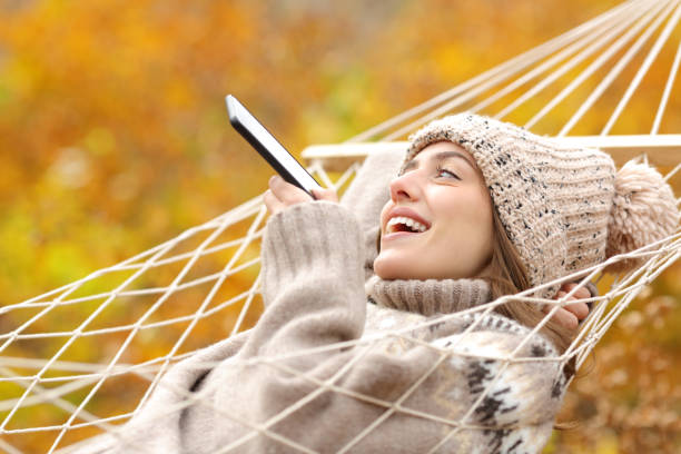 istock Happy lady on hammock dictating message on phone in fall 1291491351