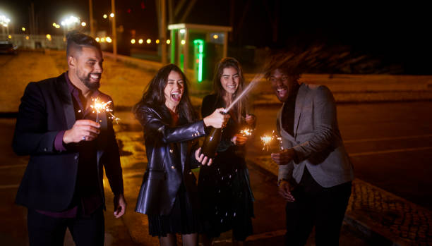 Girl opens champagne with friends celebrating with sparklers at night