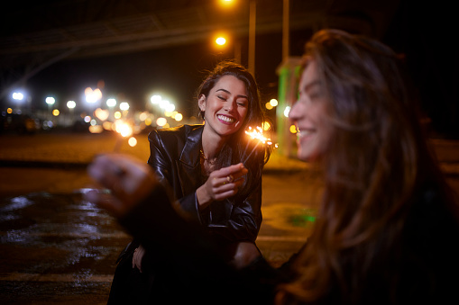 Two young girls holding sparklers celebrating at night sitting on streets