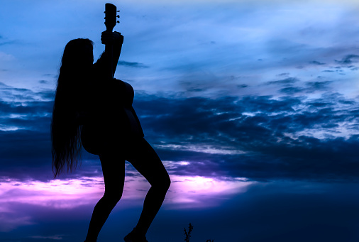 Silhouette of a woman with a guitar against the backdrop of the sunset