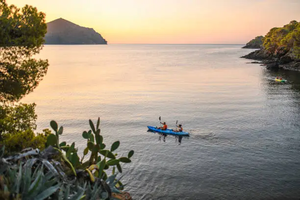 High angle tranquil scene of tandem kayak traveling along the Costa Brava in calm Mediterranean waters at sunrise.
