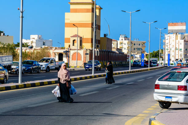 donna musulmana araba non identificata in hijab che attraversa la strada con borse della spesa nel distretto di dahar (città vecchia della città di hurghada), egitto - clothing east africa color image colors foto e immagini stock