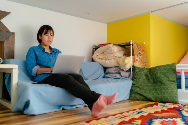 Young woman using laptop at small apartment A young woman is using a laptop at a small apartment. japan small apartment stock pictures, royalty-free photos & images