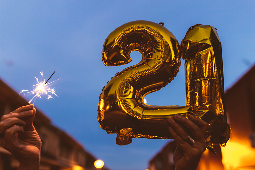 Celebrating with Gold foil balloons numeral 21 and sparkler at night. Happy New year 2021 celebration.