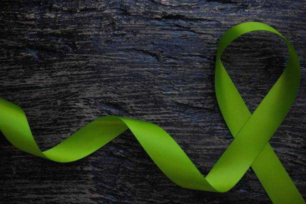 top view of lime green color ribbon on dark background. non-hodgkin lymphoma cancer, lyme disease, muscular dystrophy and postpartum depression awareness concept. - non hodgkin lymphoma imagens e fotografias de stock