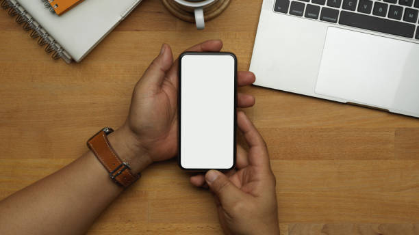 istock Male hands using smartphone on wooden worktable in office room 1291517351