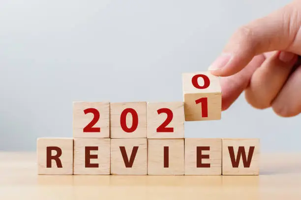Photo of 2021 review concept. Hand flip wood cube change year 2020 to 2021 and the word REVIEW on wooden block on wood table