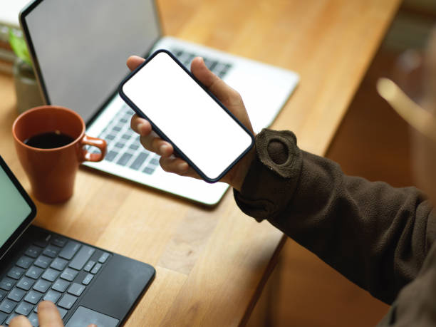 istock Male hand holding smartphone while working with laptop and tablet in office room 1291521788