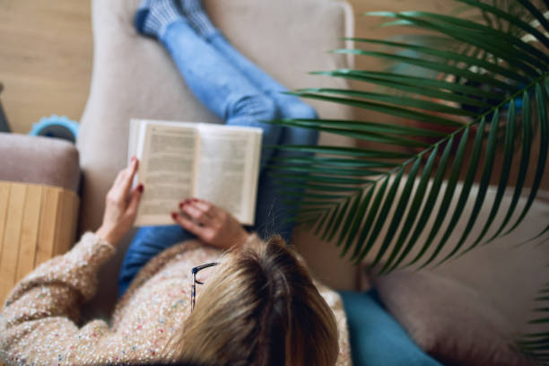 istock Young woman reading book, close-up, on home interior background 1291532647