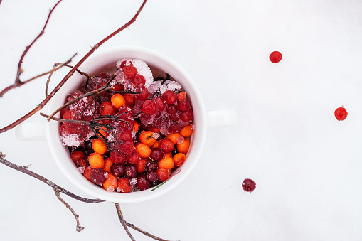 Rowan,viburnum, cranberry and sea buckthorn berries in a white mug standing on the snow.Winter concept.Natural vitamins.Top view,copy space