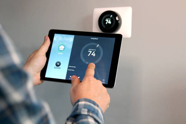 Man is Adjusting a temperature using a tablet with smart home app in modern living room Man is Adjusting a temperature using a tablet with smart home app in modern living room smart thermostat stock pictures, royalty-free photos & images