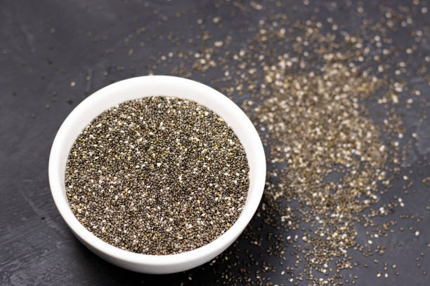 黒い石の背景に白いボウルに暗いチアの種。スペインセージの小粒 - tablespoon chia healthy eating seed ストックフォトと画像