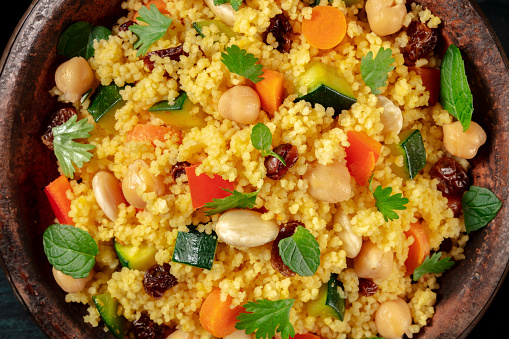 Couscous with vegetables, almonds, raisins, and herbs, close-up overhead shot in a tagine