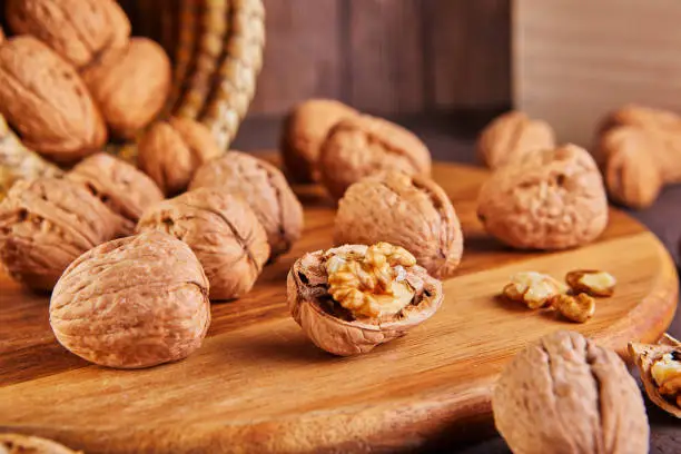 Photo of Walnuts in a wicker basket, whole and finely chopped, next to the filling and shells on a wooden background. Home storage of winter preparations