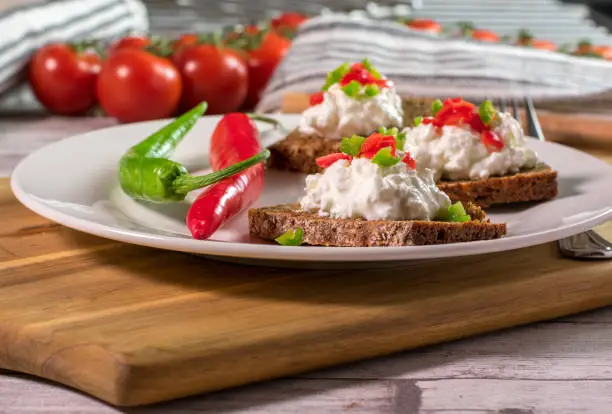 healthy vegetarian meal with cottage cheese, whole grain bread and spicy pepperonis served as a sandwich on a white plate on wooden board. Bright color image