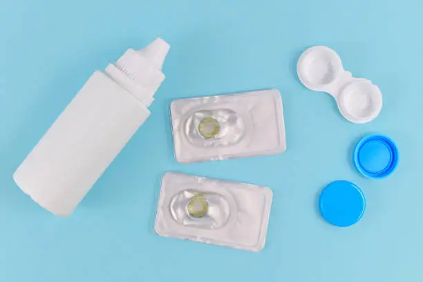 Packs with hazel colored circle lenses, a type of contact lenses to enlarge eyes and change eye color with storage container and cleaning solution on blue background