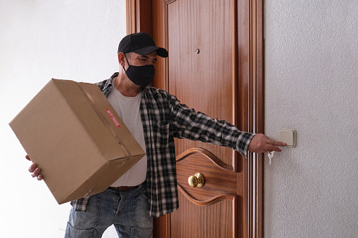Un anciano que toca el timbre de la puerta sosteniendo un paquete. 