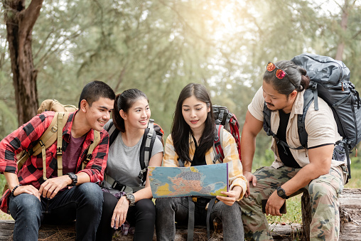 A group of young Asians are planning and looking at maps for camping in the forest.