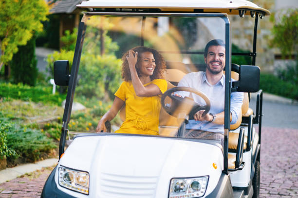 Casal se movimenta em um complexo hoteleiro e carrega bagagem em um carrinho de golfe - foto de acervo