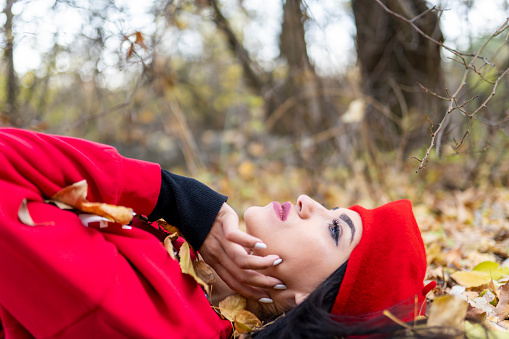 season and people concept - Portrait of beautiful young woman lying on the ground of an autumn forest with colorful maple leaves.