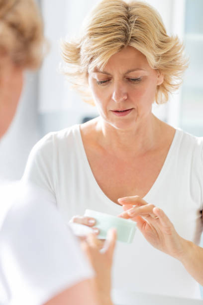 istock Blond woman's reflection in the mirror, picking face cream from jar 1291572093