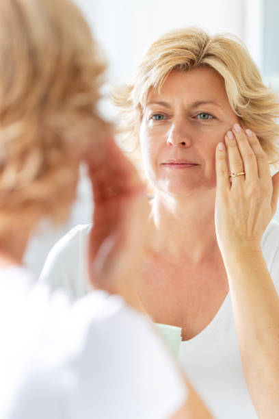 istock Blond woman's reflection in the mirror, applying face cream on cheeks 1291572094