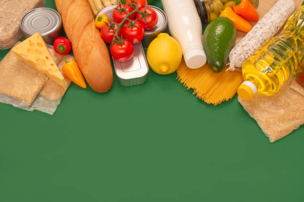 istock Different groceries, food donations on green background with copyspace - pasta, fresh vegatables, canned food, baguette, cooking oil, tomatoes, cheese. Food bank, food delivery concept 1291573508