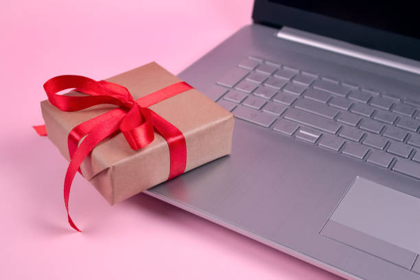 istock Front view on laptop computer and present box with red bow on pastel pink background with copyspace for your text. Seasonal sale, black friday and cyber monday concept. Online shopping 1291574309
