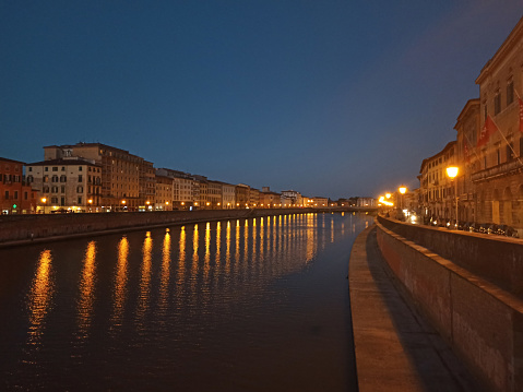 Pisa, view from the bridge over the Arno River at sunset in the evening. Historical center with reflection of lantern lights in river Arno.
