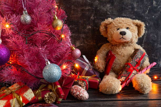 istock Atmospheric Christmas or New Year composition, pink christmas tree on black background, teddy bear, gifts. Copy space 1291578581