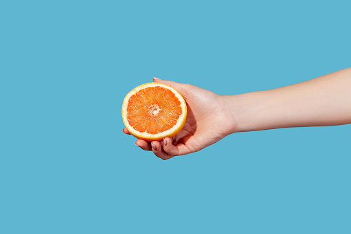 Close up side view female hand holding half of ripe juicy grapefruit, orange or pomelo, source of vitamins, healthy eating, fat burning