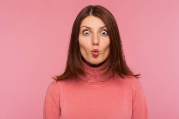 Closeup portrait attractive brunette woman in pink sweater fooling around making fish lips, having fun, humor Closeup portrait attractive brunette woman in pink sweater fooling around making fish lips, having fun, humor. Indoor studio shot isolated on pink background puckering stock pictures, royalty-free photos & images