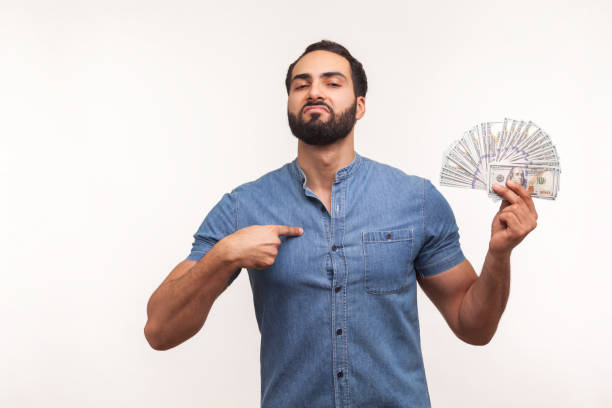 богатый бородатый бизнесмен, указывающий пальцем на себя и показывающий много долларовых банкнот, гордится своим богатством и успехом - greed currency men happiness стоковые фото и изображения