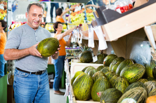Smiling male is choosing green melon in the supermarket.