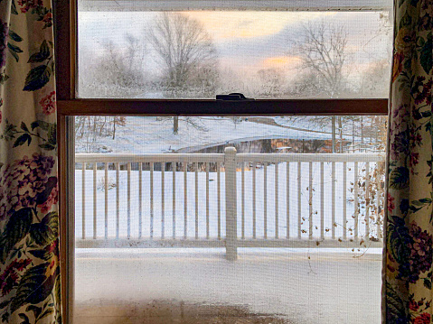 Looking out the screened window onto a snowy scene. Curtains frame the image