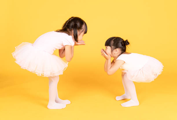 ballerina carina due bambine asiatiche che parlano rilassate dopo la lezione di balletto isolate su uno sfondo di colore giallo vibrante lucentezza brillante. due ragazze che si godono la pausa. - korea child baby asian culture foto e immagini stock