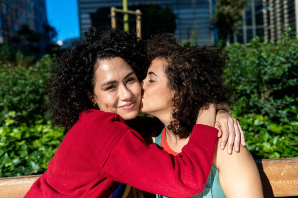 istock Smiling lesbian couple embracing and relaxing on a park bench 1291594502