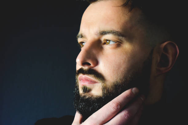 istock Man holding his beard next to a black wall 1291599029