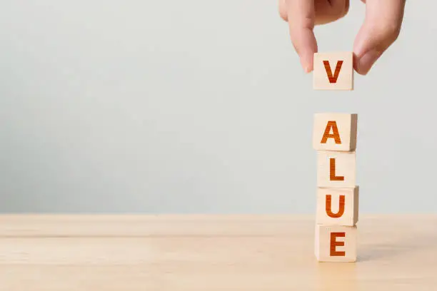 Photo of Hand of male putting wood cube block with word VALUE on wooden table