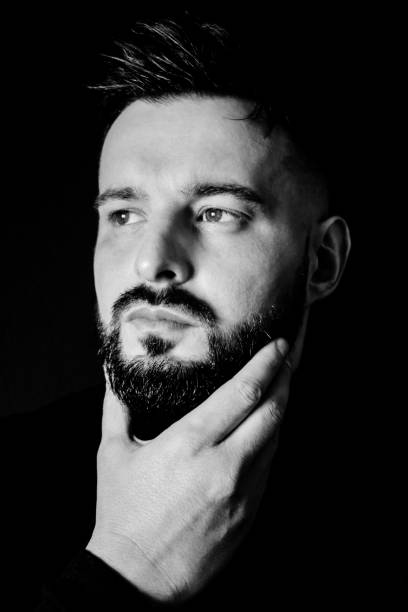 istock Man holding his beard next to a black wall, black and white 1291599853