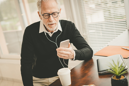 Senior businessman using earphones during conversation on mobile phone