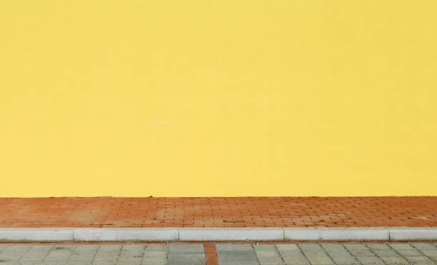 istock Yellow painted wall with a red tiled sidewalk in front. 1291605167